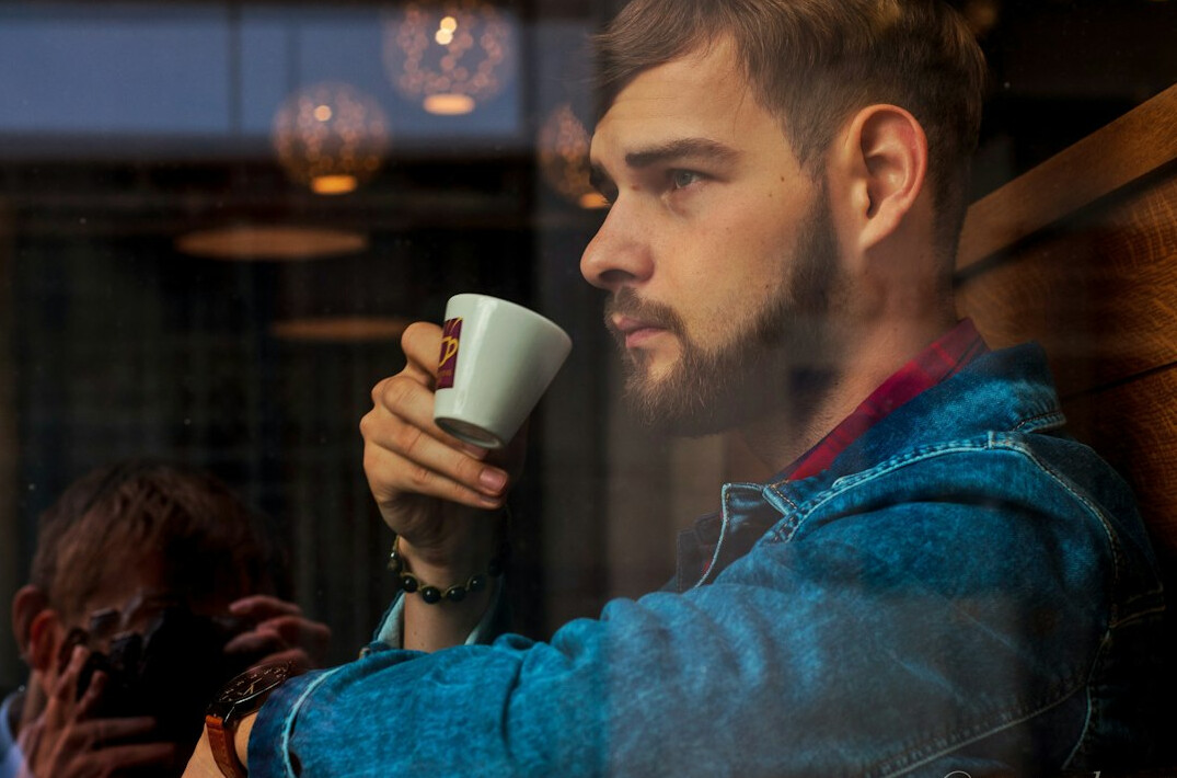 Black Canadian man sitting by a cafe window with a cup of coffee, looking outside